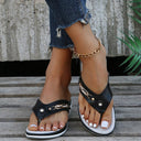 Black wedge thong sandal with perforated upper and stud embellishments, white flatform sole, worn with distressed jeans, angled front view.