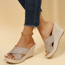 Brown cross-strap wedge mule sandals with textured woven sole, worn with dark jeans and gold ankle bracelet, angled view.
