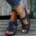 Navy floral appliqué low wedge sandals with ruffled straps, slingback ankle strap, and black sole, angled view.