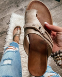 Tan brown toe-ring buckle sandal with contoured footbed, held in hand at an angle — wood surface background.