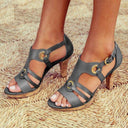 Black leather strappy high heel sandals with gold buckle details and cork heel, front angled view.