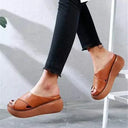Brown cross-strap platform slip-on sandals worn with dark jeans, angled side view showing raised flatform sole.