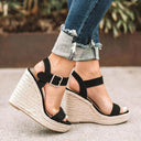 Open-toe espadrille platform wedge sandals in black suede-look with buckle ankle strap and braided cream jute platform sole, side view.