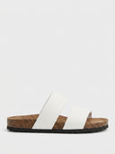 Beige two-strap flat slide sandals with cork footbed and rubber outsole, side view on white background.