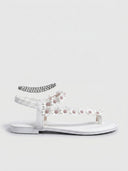White flat sandal with daisy straps, elastic ankle strap, and silver chain anklet, side view.