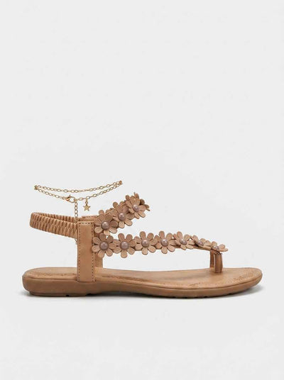 Beige flat thong sandal with daisy appliqué floral straps, pearl-centre flowers, gold chain anklet with star charm, side view on white background.