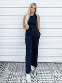 Navy sleeveless jumpsuit with drawstring waist, front view against white wall.