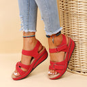 Red low wedge sandals with two adjustable strap closures, open toe and platform sole, angled front view.