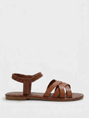 Flat brown strappy sandals with crisscross forefoot straps and gathered elastic ankle band, angled side view on white background.