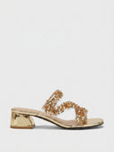 Gold sequin crossover strap block heel mules with gold pyramid-studded heel and clear strap sections, side view on white background.