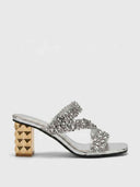 Silver sequin crossover strap block heel mules with gold pyramid-studded heel, side profile view on white background.