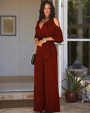 Rust-colored jumpsuit with cold shoulder detail, V-neck, and waist tie, front view outdoors.