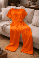 Orange wide-leg jumpsuit with short sleeves and tied belt, front view on a sofa.