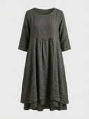 Dark green linen mini dress with 3/4 sleeves, gathered waist, and layered hem, front view on white.