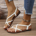 White braided strap flat sandals with cross-front rope-twist straps, toe ring and slingback ankle strap, cushioned tan footbed, worn with distressed denim jeans, angled side view.