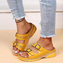 Yellow platform wedge sandals with two adjustable buckle straps and perforated floral cutout detailing on straps, angled front view.