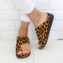 Panther print open-toe wedge mule sandals with wide toe-band and black sole, worn with white trousers, angled front view.