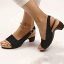 Black peep-toe slingback sandals with cork block heel and buckle ankle strap, angled side view on model wearing ankle bracelet.