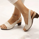Cream peep-toe slingback sandals with cork block heel and buckle ankle strap, angled side view on model.