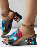 Holographic multicolor open-toe mule sandals with jewel-encrusted block heel in red, teal and amber gemstones, angled front view styled with gold chain anklets.