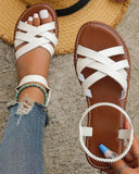 White criss-cross strap flat sandals with tan footbed and elasticated ankle loop, overhead view on feet with jeans and beaded anklet.