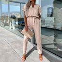 Beige short-sleeve jumpsuit with a belted waist, V-neck, and gold detail, front view.