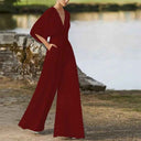 Red dolman sleeve knit jumpsuit with V-neckline and pockets, angled front view by water.