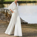 White dolman sleeve jumpsuit with V-neck, cinched waist, and wide legs, angled view outdoors.
