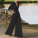 Black dolman sleeve knit jumpsuit with V-neckline, angled view by a lake.