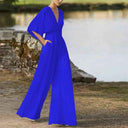 Royal blue dolman sleeve knit jumpsuit with V-neckline and pockets, angled view by water.