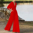 Red dolman sleeve knit jumpsuit with V-neckline and pockets, angled view by a lake.