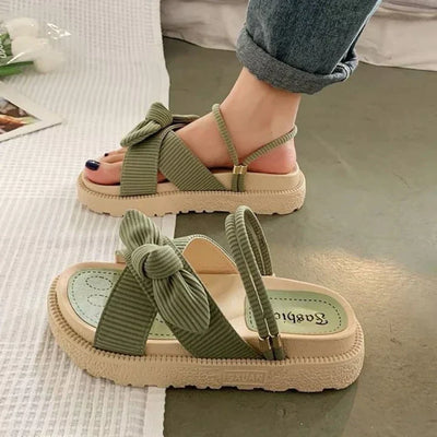 Sage green ribbed fabric flatform sandals with oversized bow knot detail and beige crepe sole, worn as slingback, angled view.