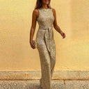 Silver sequin sleeveless jumpsuit with tie waist, front view against yellow wall background.
