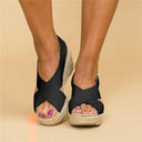 Black espadrille wedge sandals with wide cross-strap upper and braided jute sole, worn on feet with purple nail polish, front angled view.