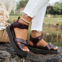Burgundy chunky platform sandals with crossover straps and buckle ankle strap, worn with white distressed jeans, angled view.