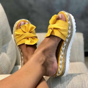 Yellow platform wedge sandals with fabric bow detail and woven braided sole, open-toe slip-on, worn on feet angled view.