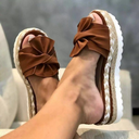 Brown platform wedge sandals with fabric bow detail, woven midsole and cream textured rubber outsole, angled side view.