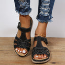 Black flatform sandals with woven crossover open-toe upper, white contrast topstitching and hook-and-loop ankle strap, front view on feet.