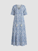 Blue and white ikat print maxi dress with V-neck and tassels, front view on gray background.