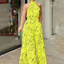 Lime green halter jumpsuit with black abstract print, front view on a street.
