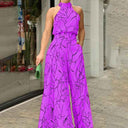 Purple halter jumpsuit with black abstract face print, front view, urban background.