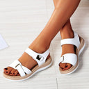 White low wedge sandals with two broad crossover straps, velcro-tab closure and cushioned beige platform sole, worn on feet, angled front view.
