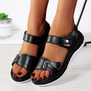 Black low wedge sandals with dual adjustable straps, metal-trim buckle detail and white wedge platform sole, front angled view on model.