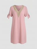 Pink V-neck knee-length dress with gold crochet trim and tied sleeves, front view on a gray background.