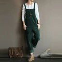 Dark green corduroy sleeveless jumpsuit with side pockets, front view on a gray background.