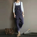 Gray corduroy sleeveless jumpsuit with side pockets, worn over a white long-sleeve shirt, full-body view.