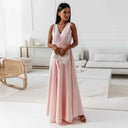 Pink sleeveless deep V-neck maxi gown with tie waist, front view in a modern room.