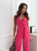 Fuchsia sleeveless jumpsuit with V-neck and tie waist, angled view on white background.