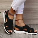 Black mesh low wedge sandals with white cushioned sole, cutout upper panels and open toe, angled side view.