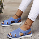 Periwinkle blue mesh low wedge sandals with white cushioned sole and velcro slingback strap, angled view on wooden background.
